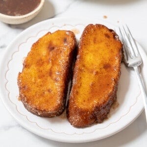 two torrijas on a white plate with a fork.