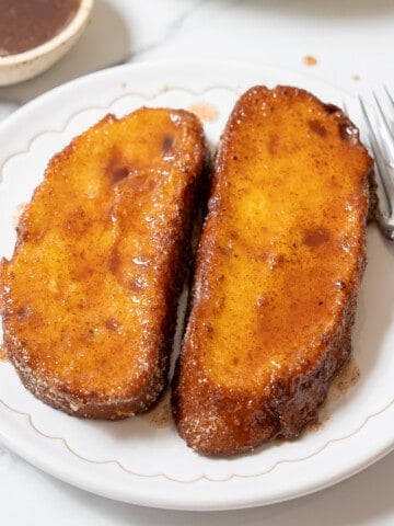 two torrijas on a white plate with a fork.