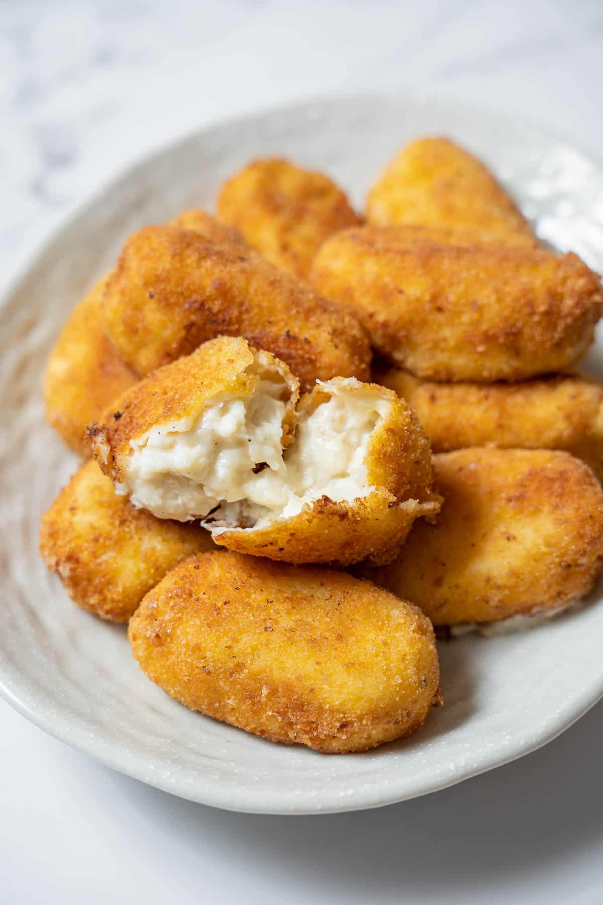 a plate of cod croquettes with one broken in half.