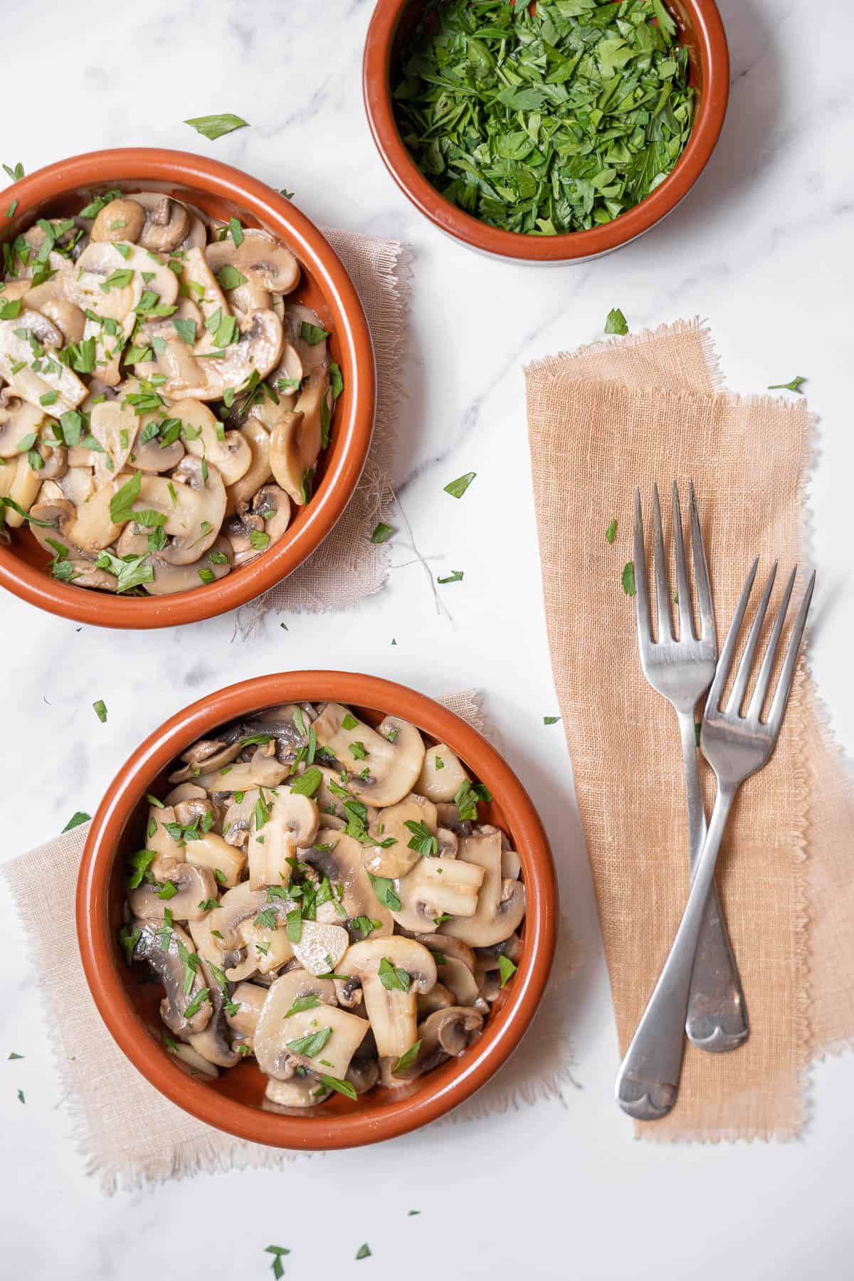 two bowls of garlic mushrooms with two forks.