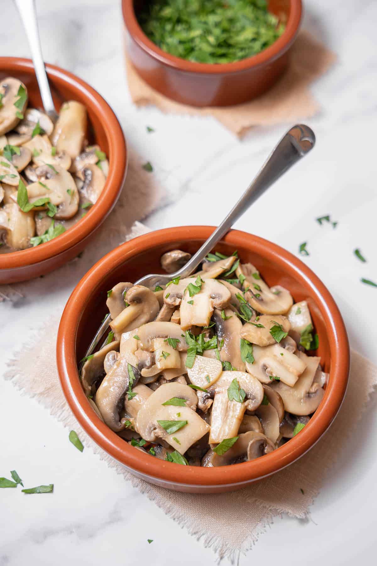 serving two bowls of garlic mushrooms with parsley.