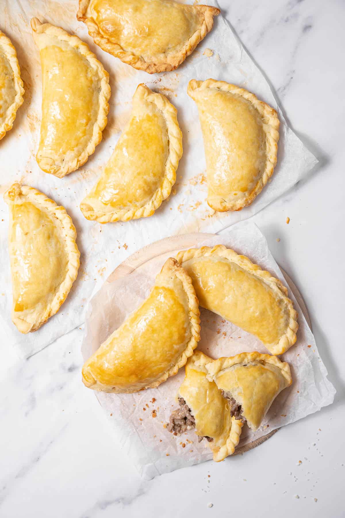 baked empanadas on a plate and on a parchment paper.