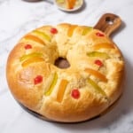 loaf of roscón de reyes on a round cutting board.