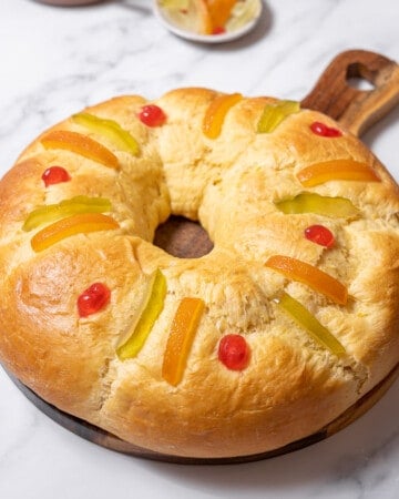 loaf of roscón de reyes on a round cutting board.