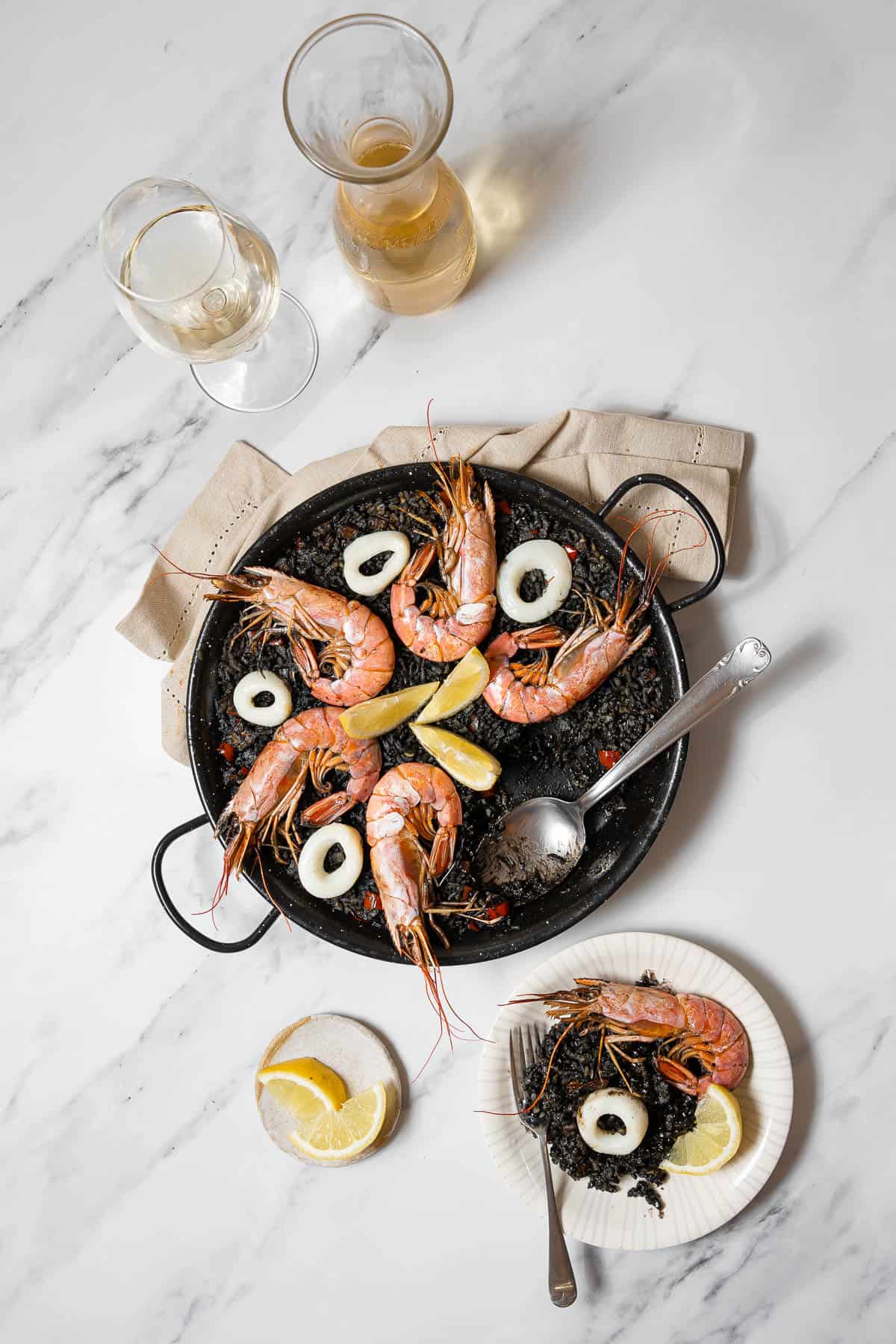 serving the black paella on a white plate.