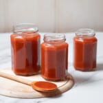 three jars of salsa de tomate with a wooden spoon.