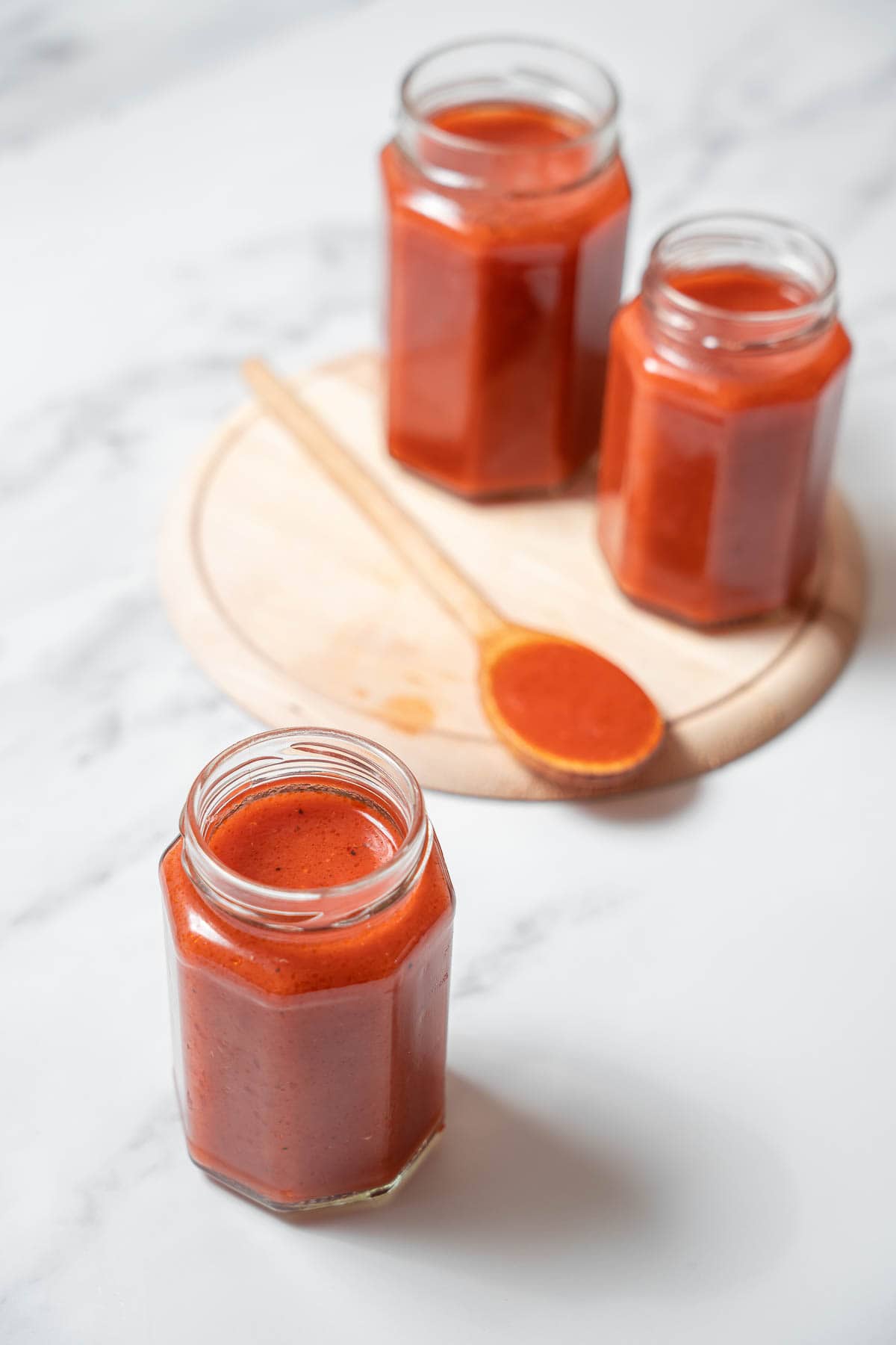 three glass jars of tomato sauce with a wooden spoon.