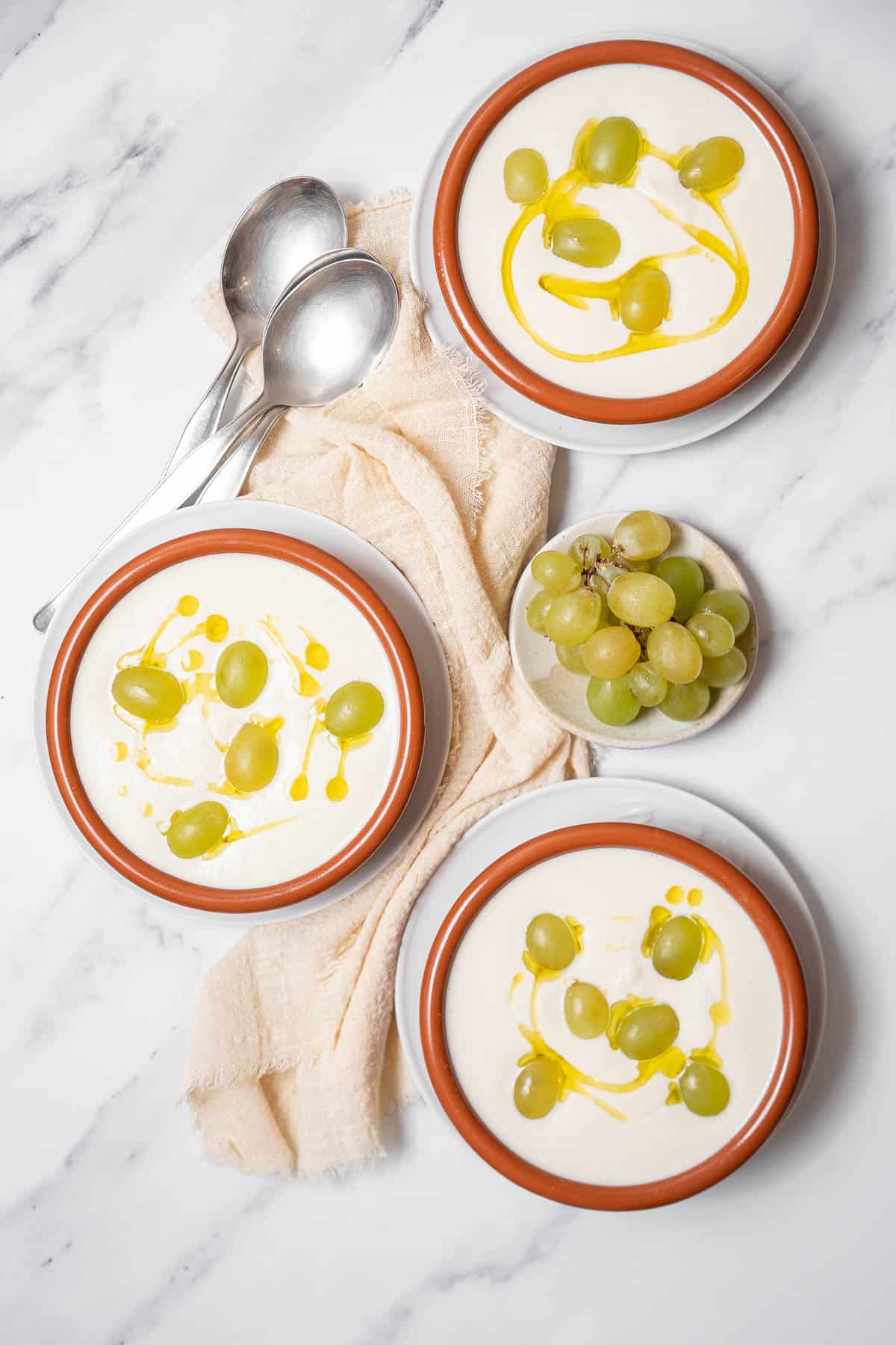 three bowls of ajo blanco with grapes and spoons.