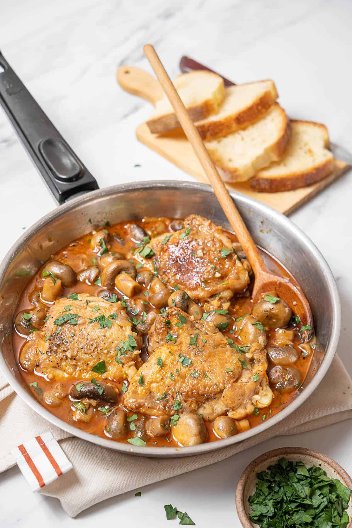 pan of chicken with mushrooms with a wooden spoon.