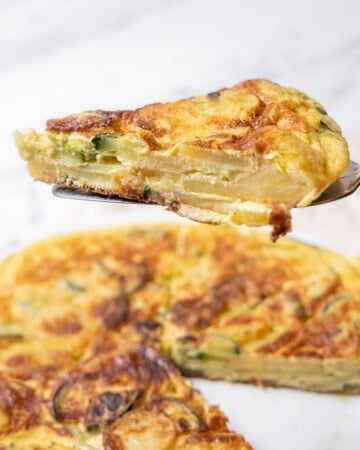holding a slice of Spanish tortilla with zucchini.