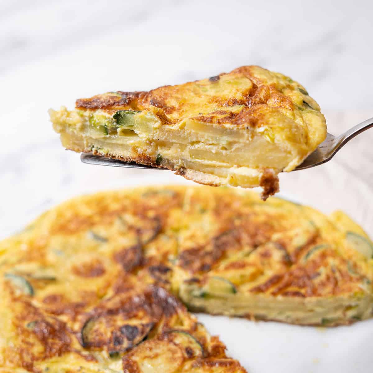 holding a slice of Spanish tortilla with zucchini.