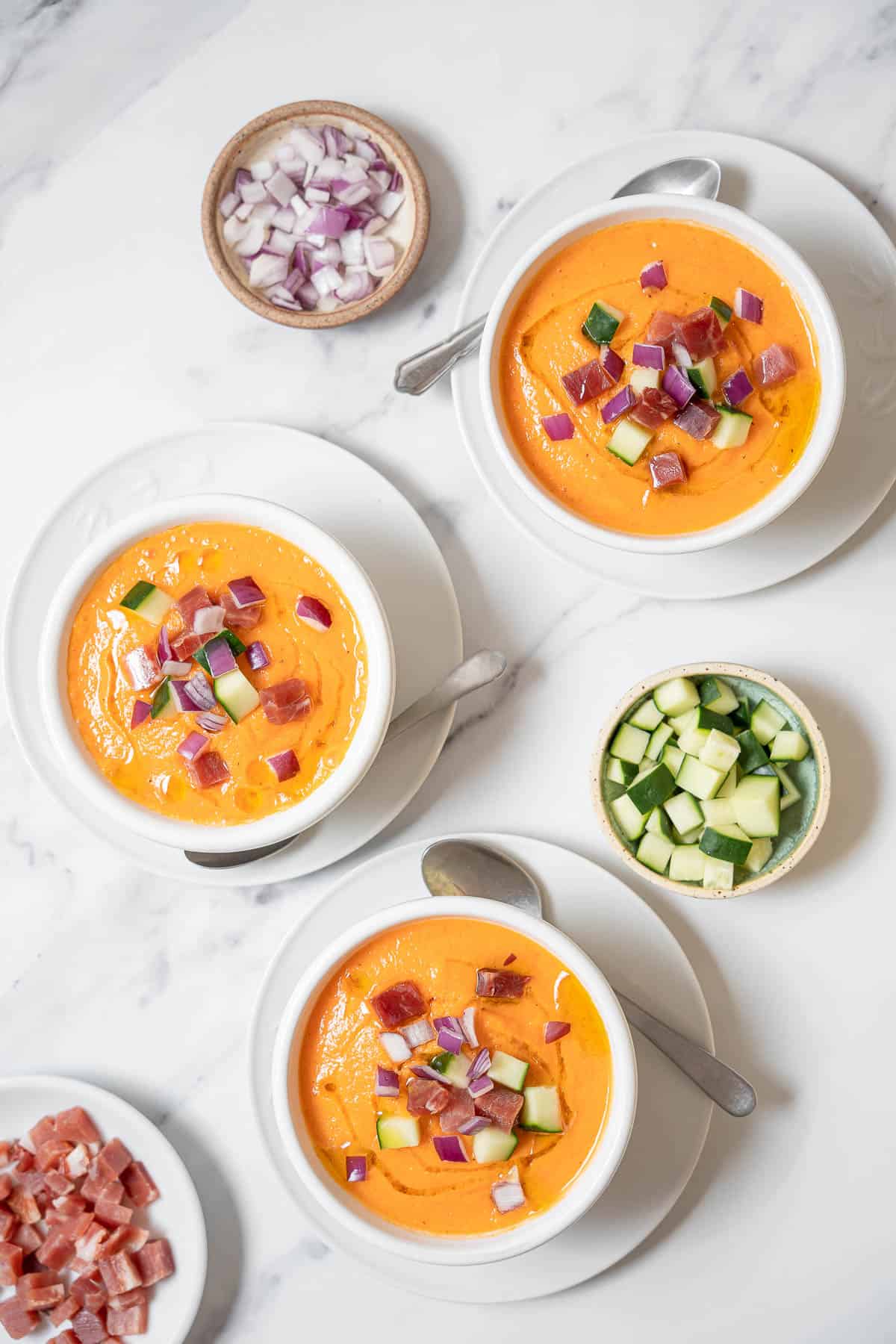 three bowls of gazpacho with toppings.