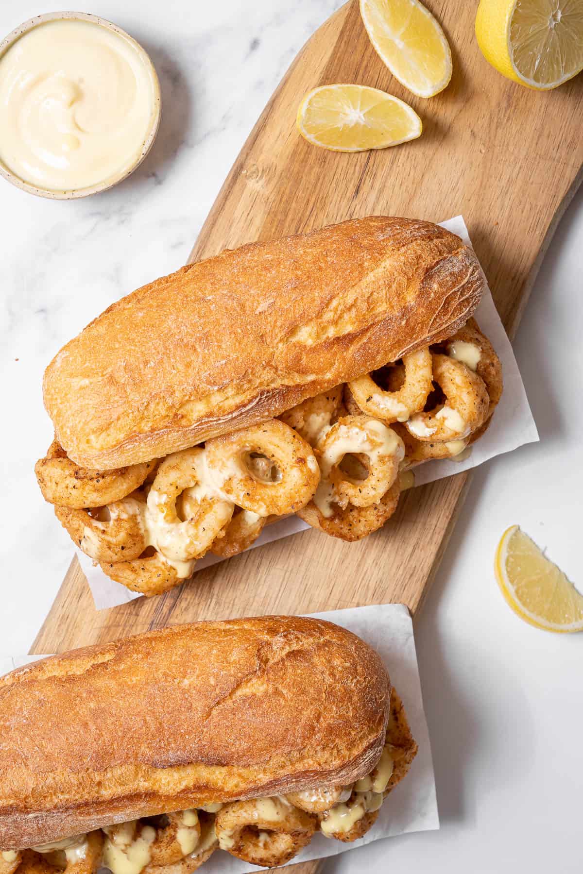 two fried calamari sandwiches with lemon wedges.