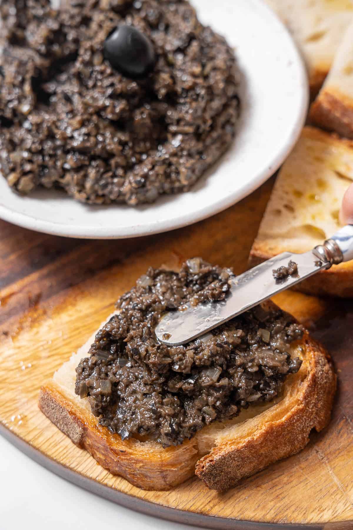 spreading black olive tapenade on bread.