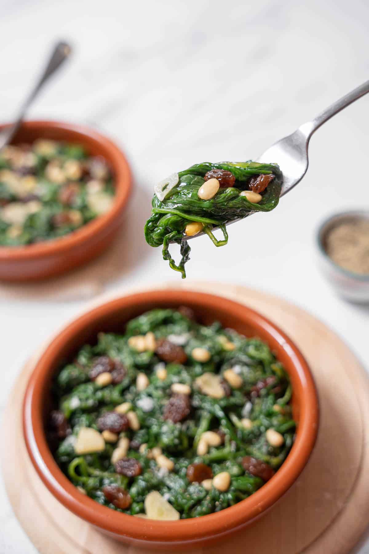 holding a forkful of spinach with pine nuts.