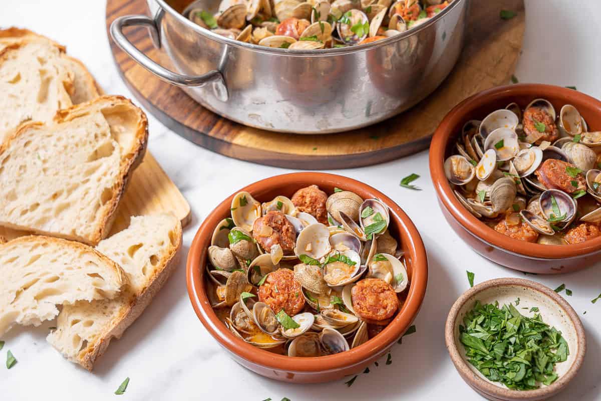 bowls of clams and chorizo with sliced bread.