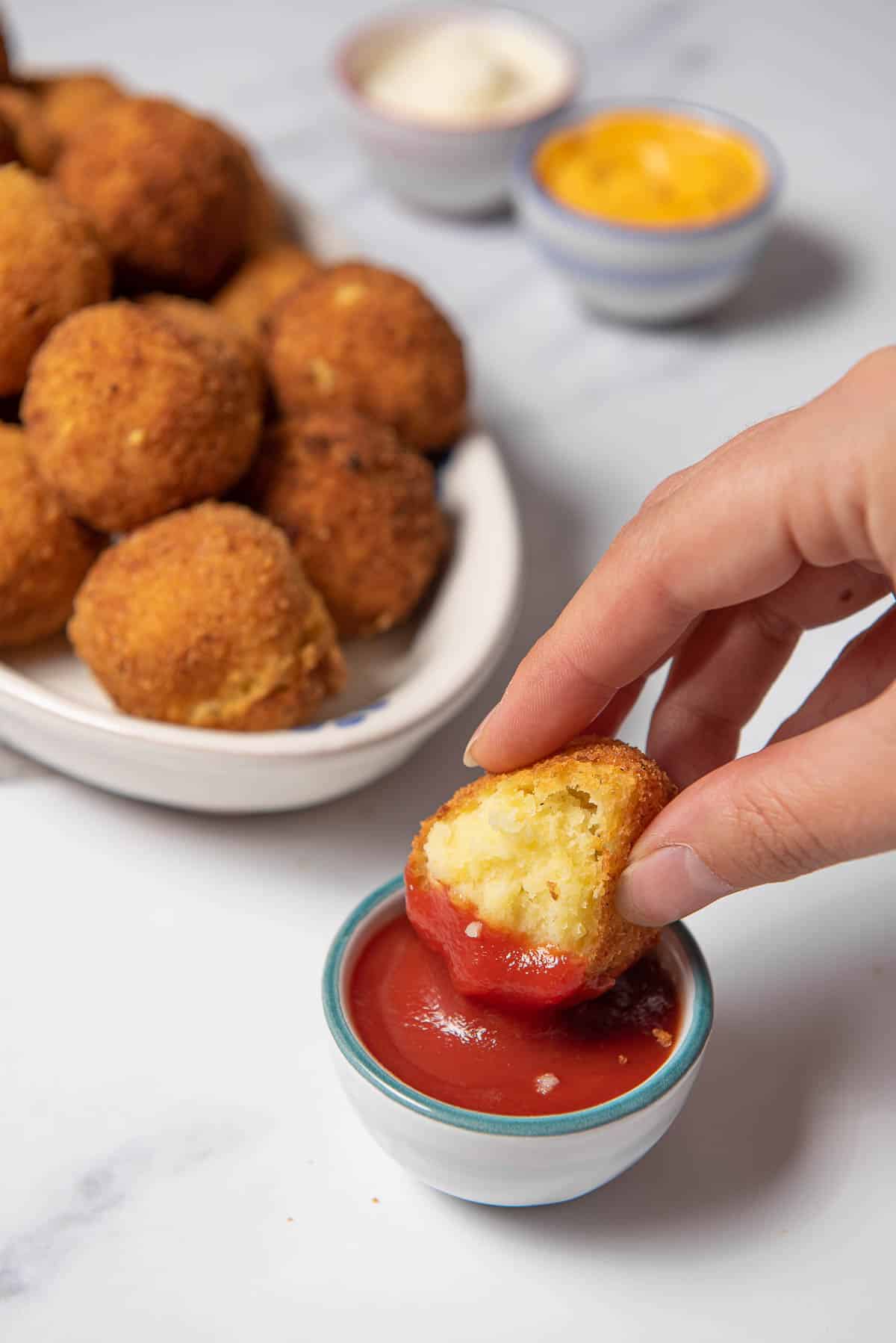 dipping a potato croquette into a red sauce.